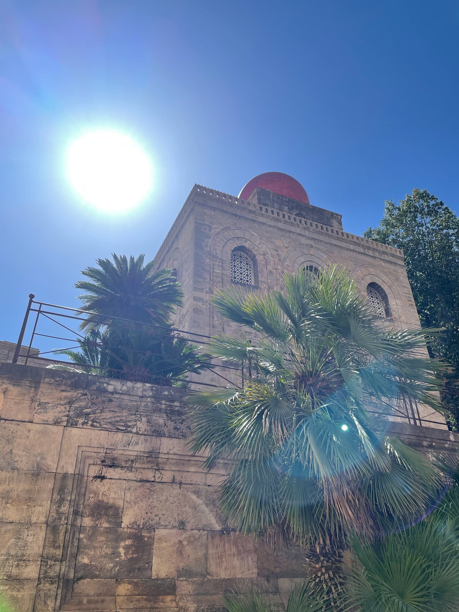 Palm trees pictured in front of an ancient Sicilian church in central Palermo on a sunny day.
