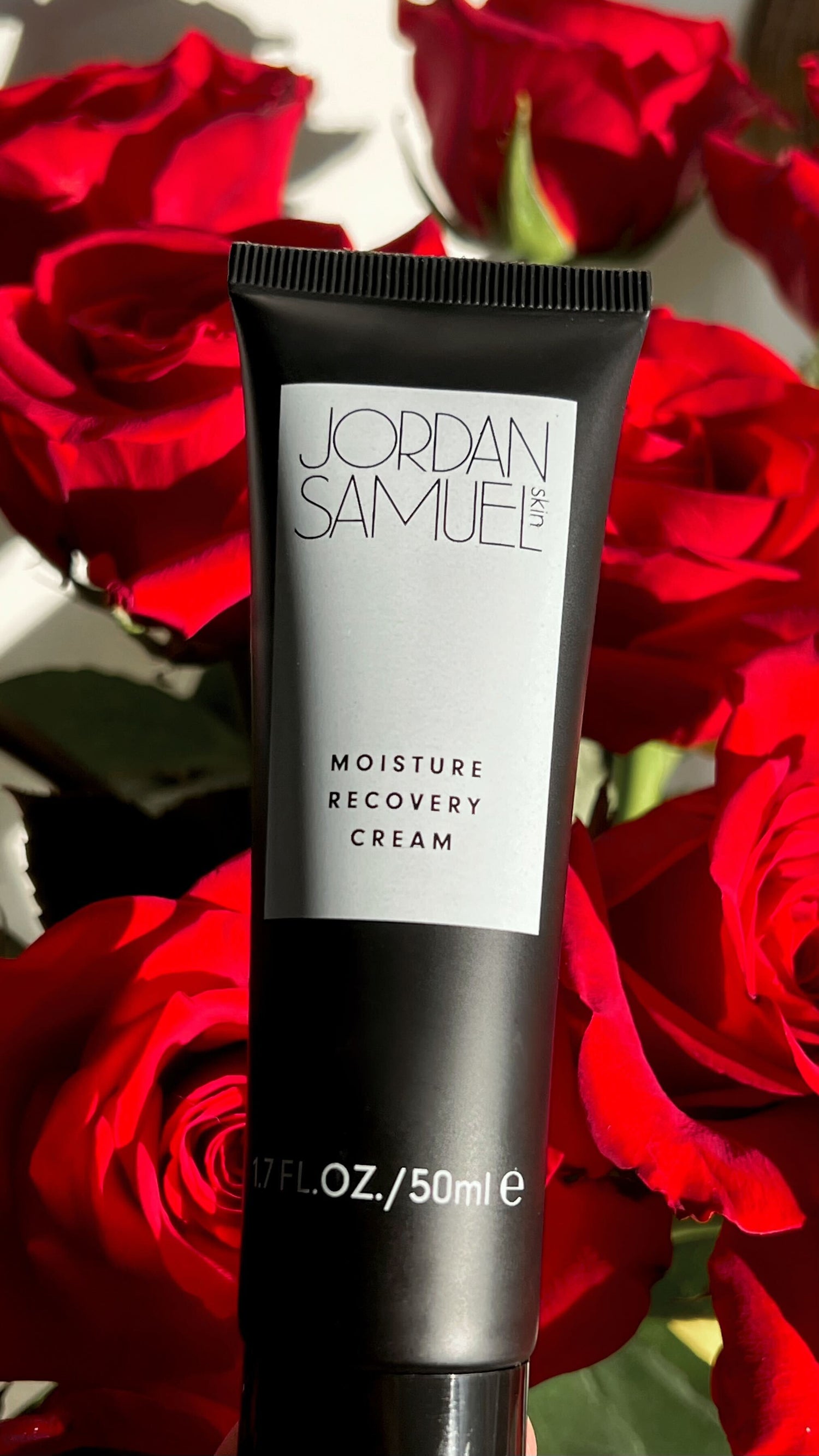 Moisture Recovery Cream's black tube with white label held over beautiful and vibrant red roses.